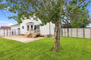 Expansive backyard featuring a concrete patio, wood deck with stairs, a bay window, and a chain-link fence with privacy slats