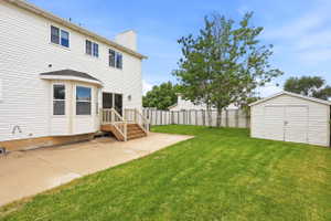 Expansive backyard with a manicured lawn, a concrete patio, and a storage shed