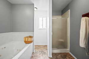 Spacious bathroom featuring a built-in jetted tub, a separate shower enclosure with a clear glass door, and neutral gray walls
