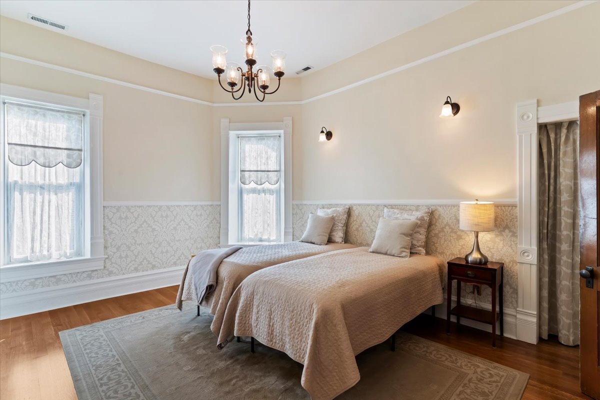 Bedroom featuring hardwood flooring, two windows with decorative trim, a two-tone wall with patterned wainscoting, and a chandelier