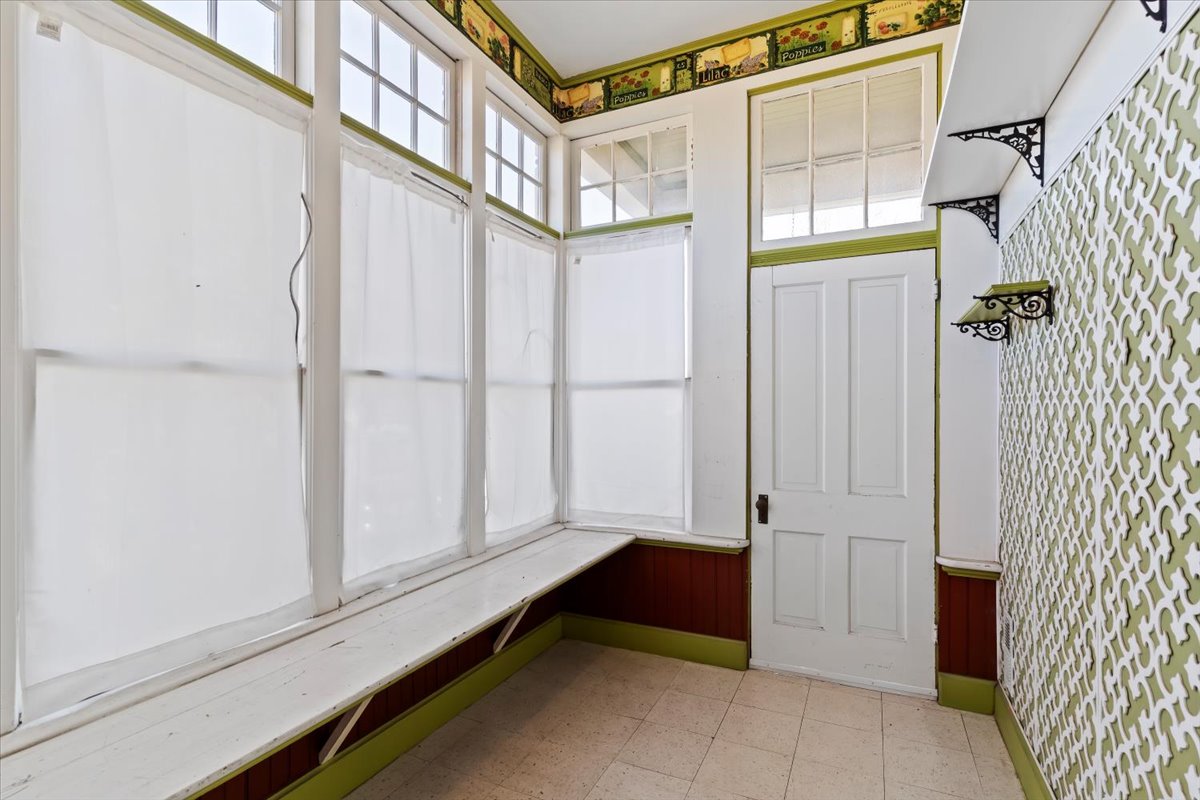 Enclosed porch featuring multiple windows with upper transoms, a built-in bench, tiled flooring, and a decorative wall panel