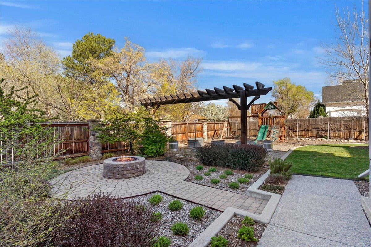 Expansive backyard featuring a circular paver patio with a stone fire pit, a wood pergola structure, a wooden privacy fence, and a green lawn area