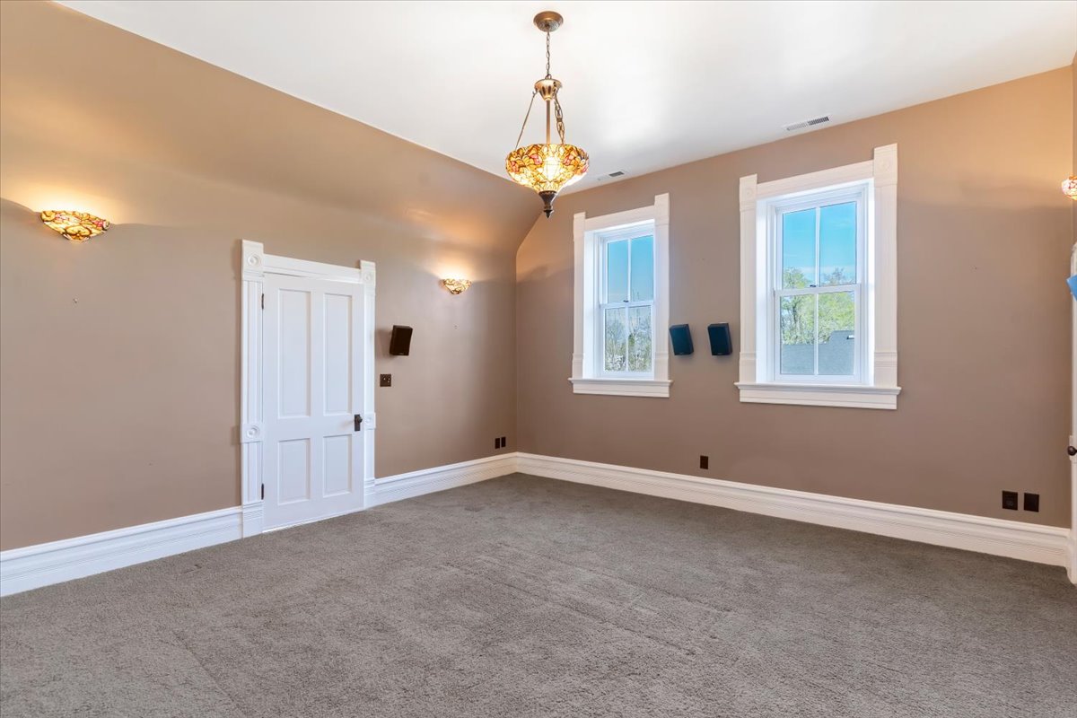 Carpeted room featuring two double-hung windows with decorative white trim, a paneled door, and three ornate sconces