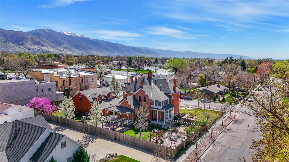 Expansive aerial capturing a prominent brick Victorian-style residence with a multi-gabled roofline and a wrap-around porch