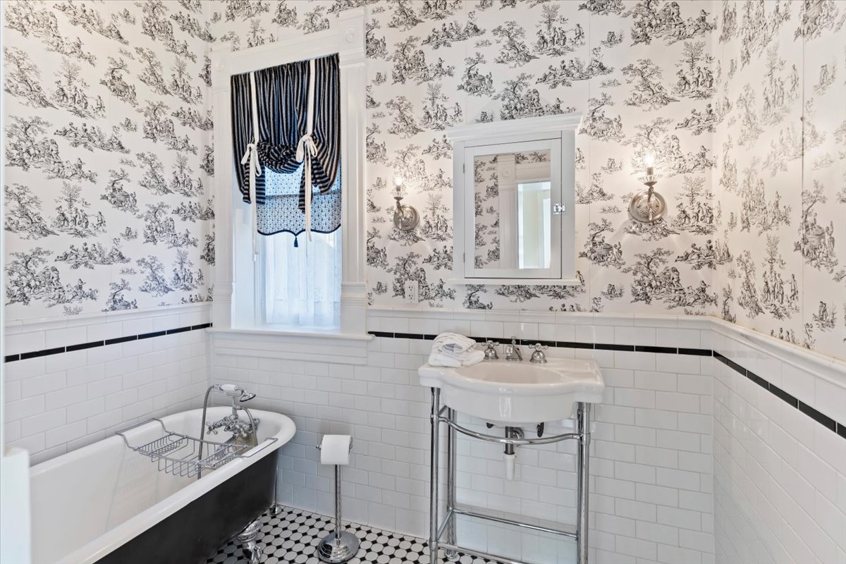 Bathroom featuring black and white toile wallpaper, white subway tile wainscoting with a black accent band, and black and white mosaic floor tiling