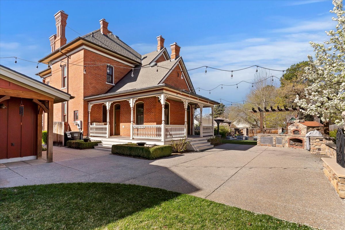 Victorian brick exterior featuring a covered porch with white railings, multiple chimneys, and an adjacent red-sided outbuilding
