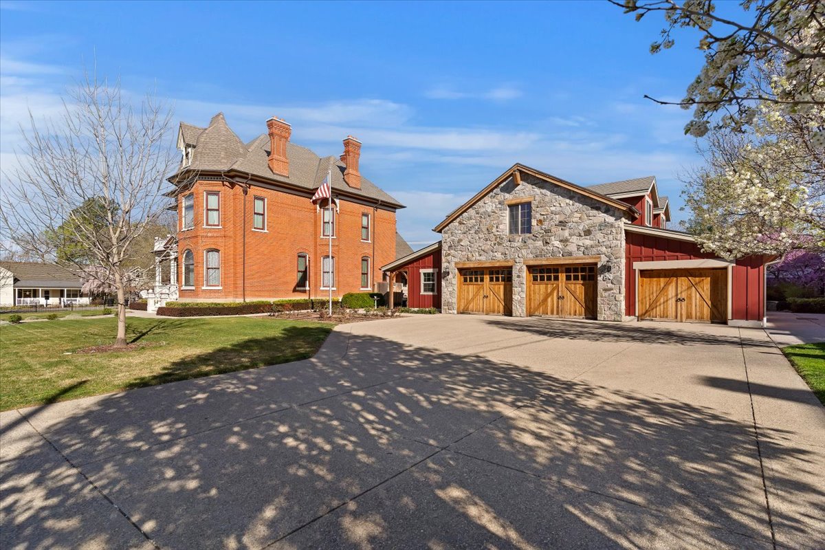 Concrete driveway leading to a three-car garage featuring stone and wood construction