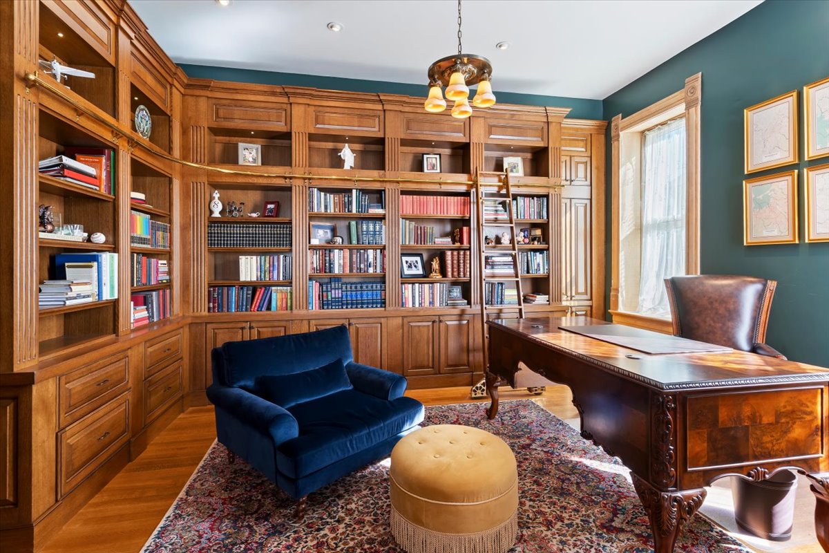 Custom wood-paneled library featuring extensive built-in shelving, a rolling ladder, window trim, and hardwood flooring