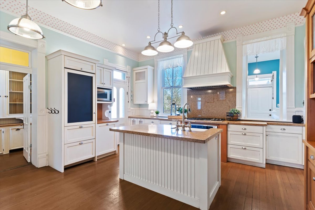 Kitchen featuring a central island with an undermount sink, white cabinetry, wood-finish flooring, a built-in microwave, and a range hood