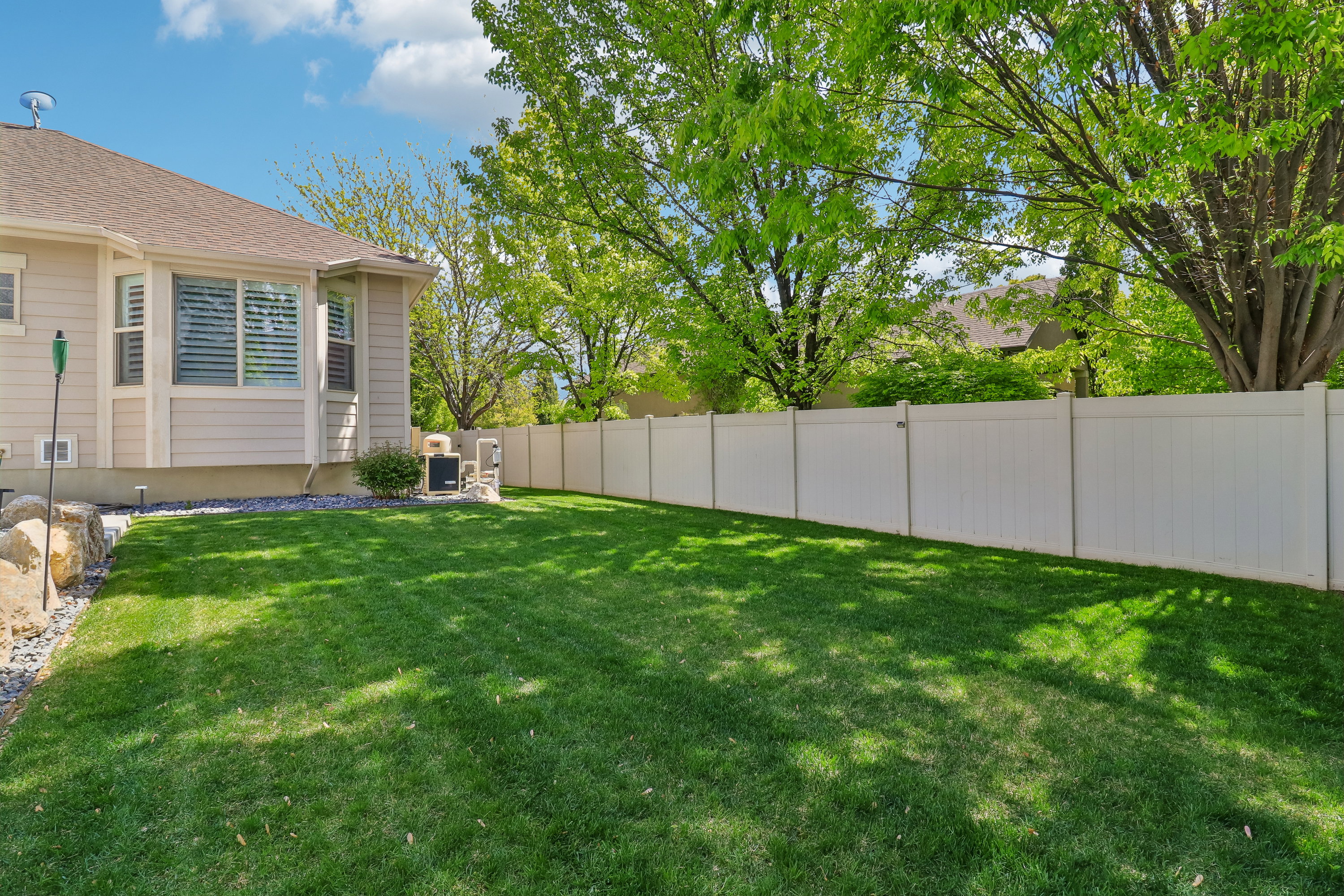 Expansive lawn area featuring a white privacy fence and mature trees