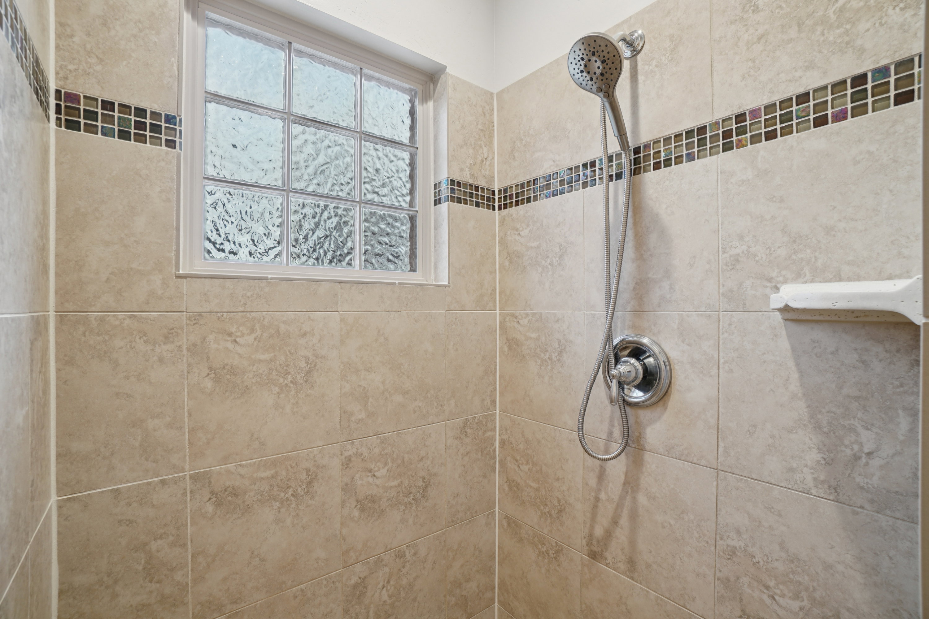 Shower enclosure with full-height neutral-toned tile, a decorative mosaic tile accent band, and a window featuring obscured glass