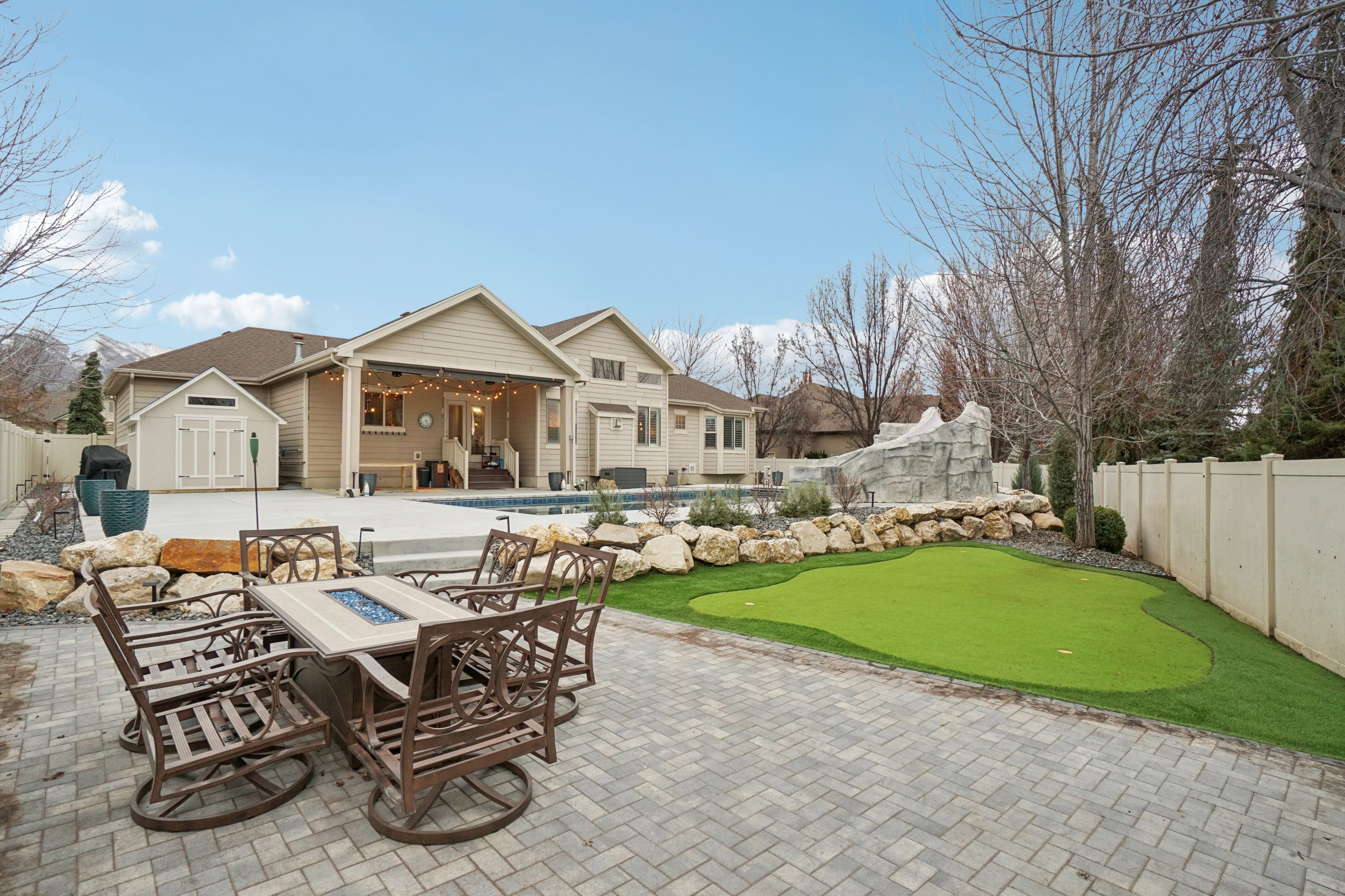 Paver patio with a built-in fire pit table, artificial turf putting green, swimming pool, and covered patio