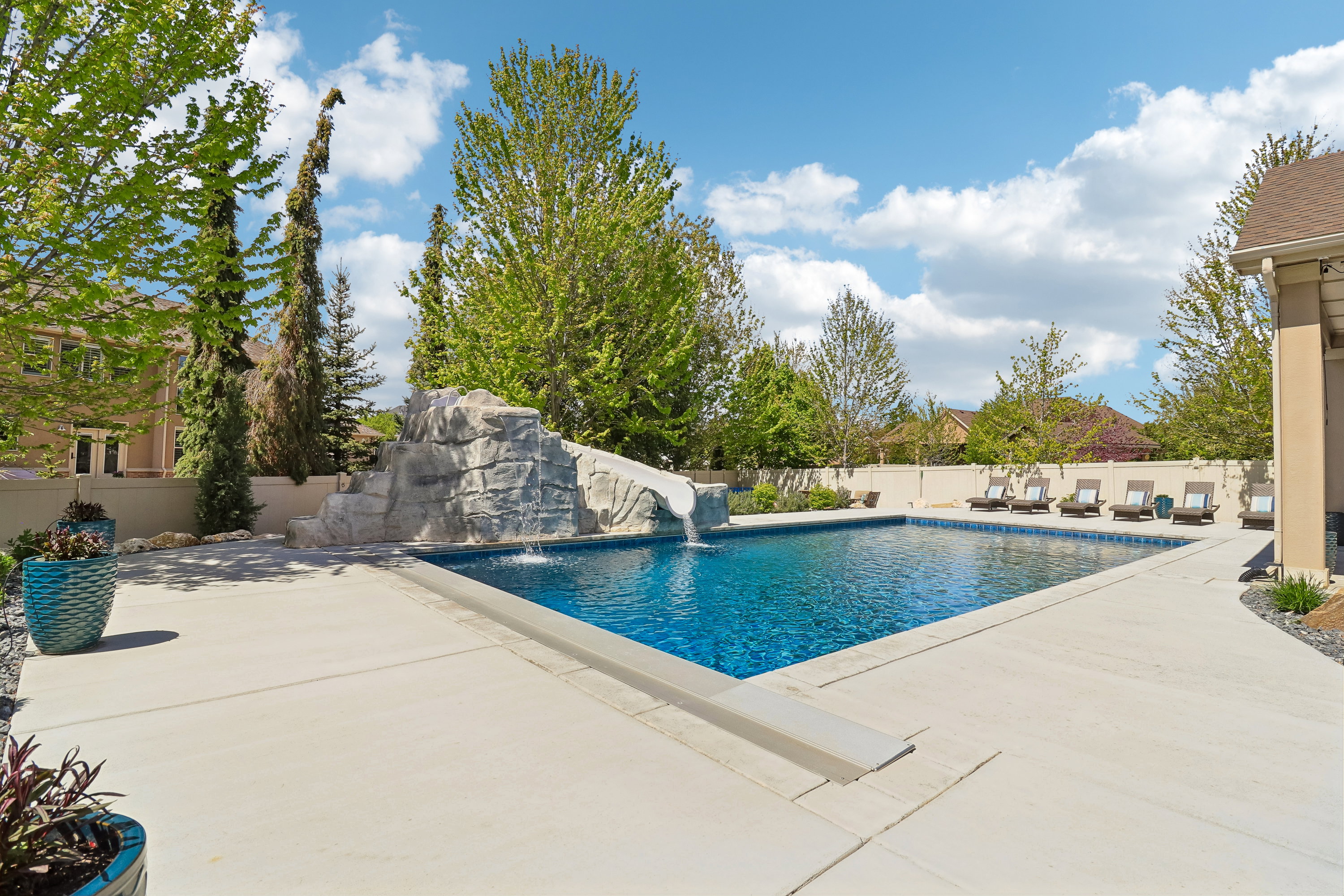 Expansive outdoor living area featuring a rectangular swimming pool with a rock water slide, a waterfall feature, and ample surrounding concrete patio space