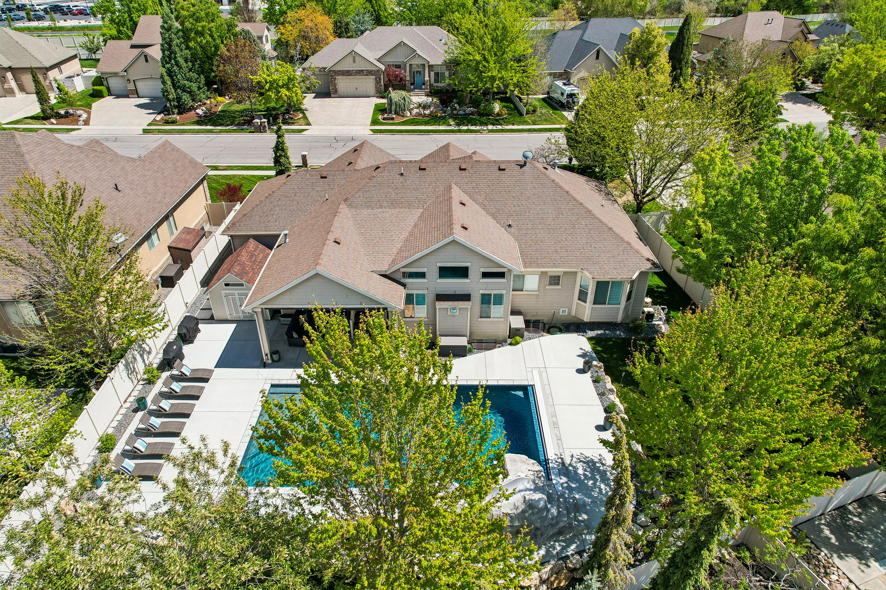 Rear exterior featuring a large in-ground swimming pool, an expansive concrete patio, a covered outdoor living area, a white privacy fence, and mature trees