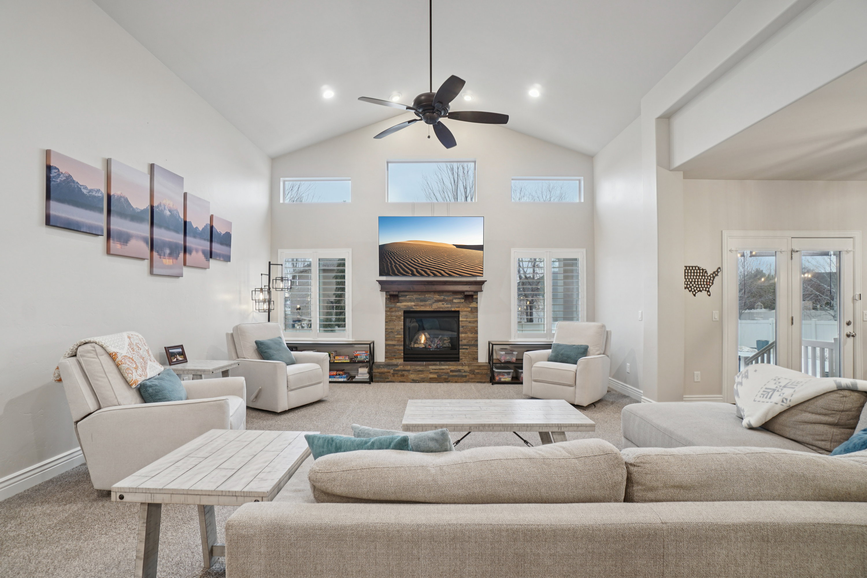 Living area featuring a vaulted ceiling with a ceiling fan, a stone-surround fireplace, and transom windows