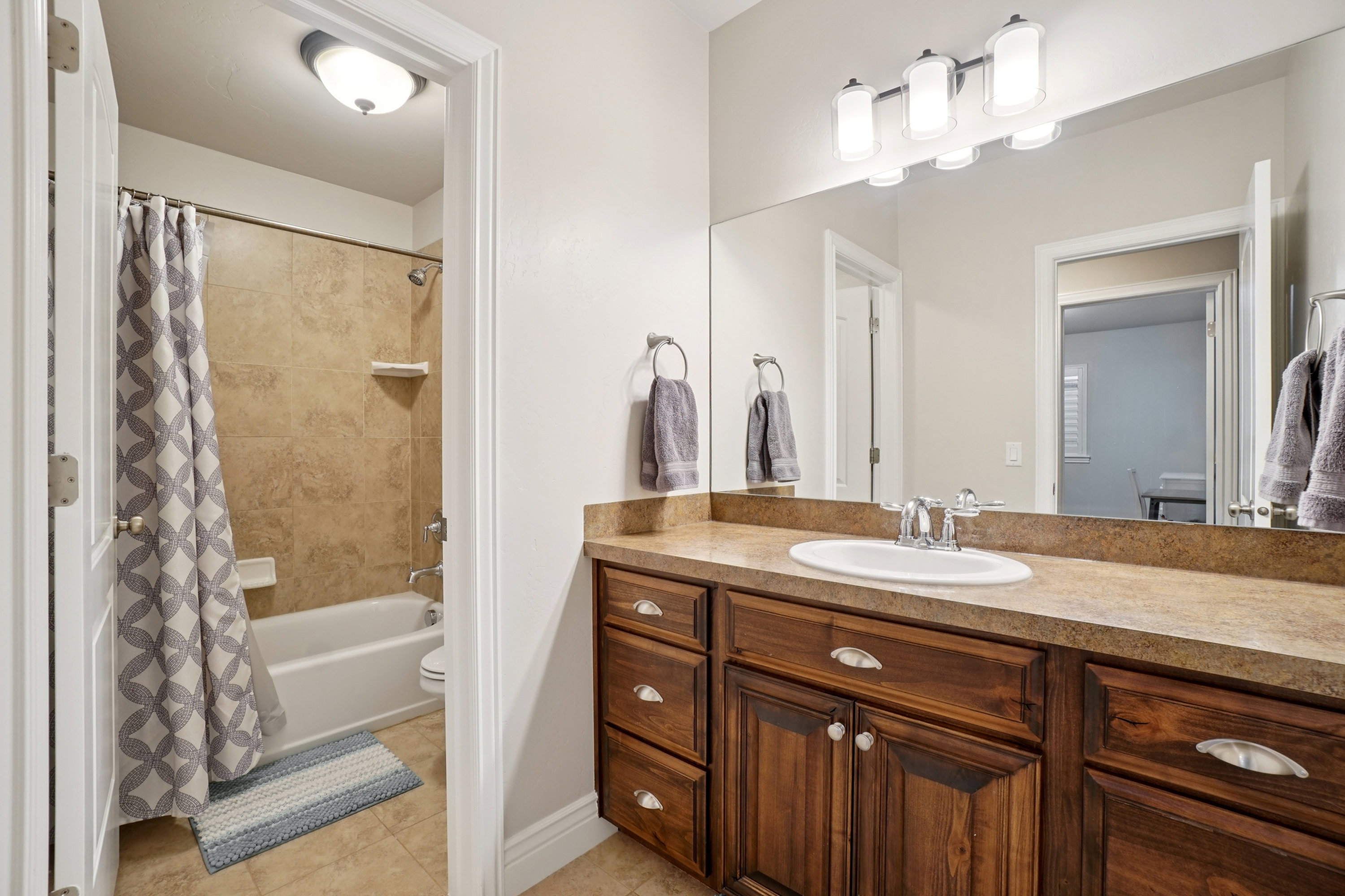 Bathroom featuring a single vanity with a white basin sink, wood-finish cabinetry, and a full-width mirror