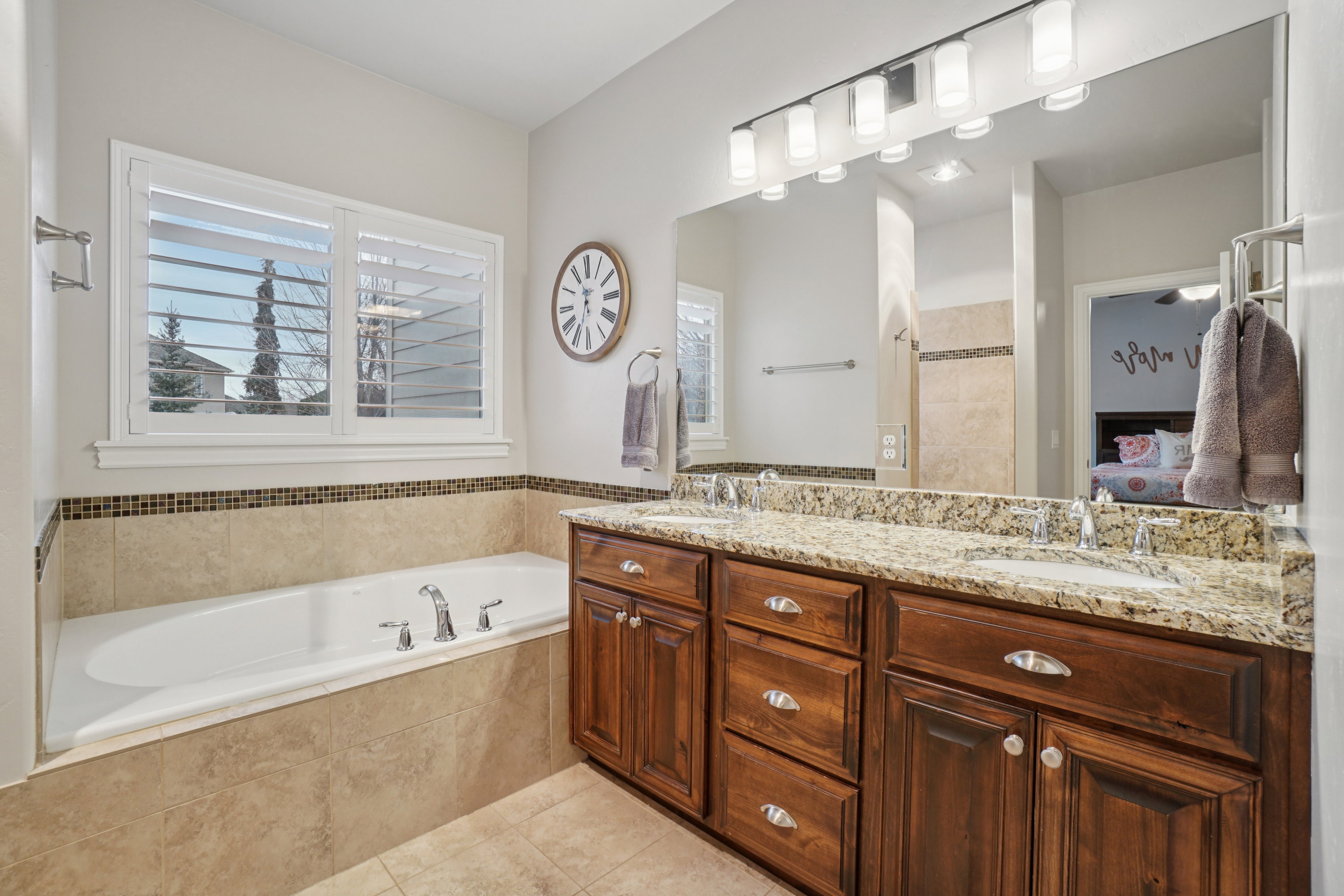 Bathroom featuring a built-in soaking tub, plantation shuttered window, and dual vanity with granite countertop