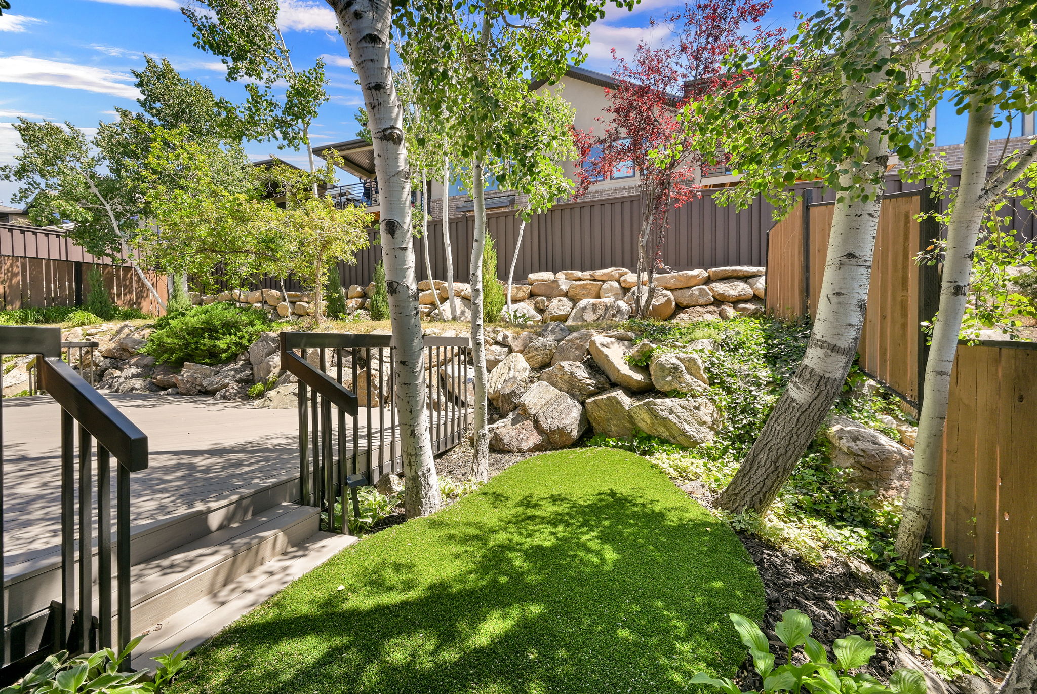 Tiered backyard with a stone retaining wall, mature trees, and a manicured artificial turf area
