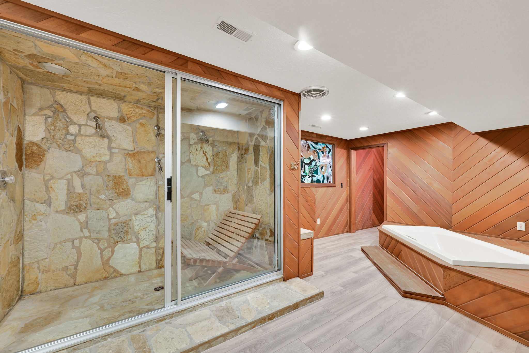Stone-tiled shower enclosure with multiple shower heads and a glass sliding door