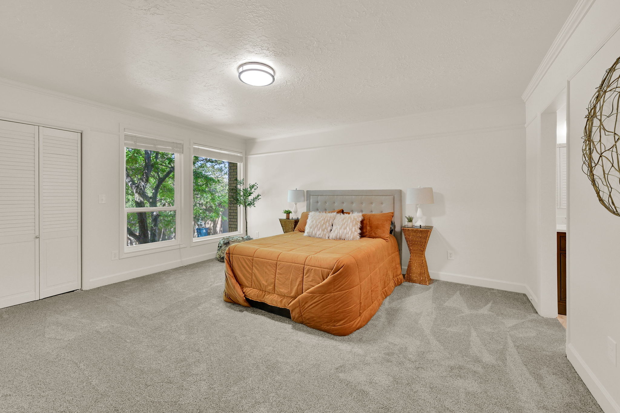 Spacious room featuring multiple windows, a ceiling-mounted light fixture, louvered bi-fold closet doors, and light gray carpeting