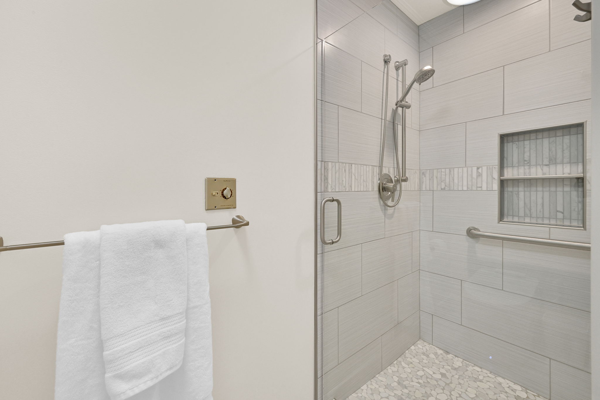 Glass-enclosed shower featuring large format tile, a decorative mosaic accent strip, and a recessed shower niche