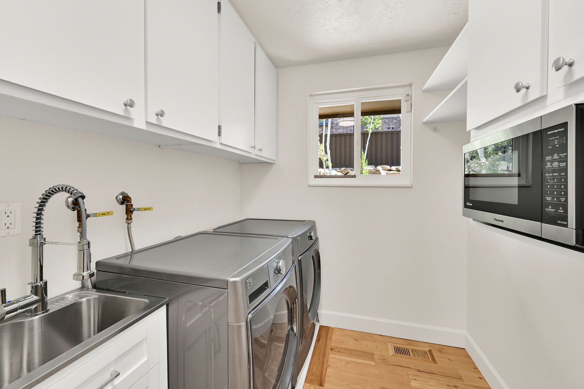 Utility space featuring white cabinetry, a stainless steel sink with a pull-down faucet, an under-cabinet microwave, and light wood-finish flooring