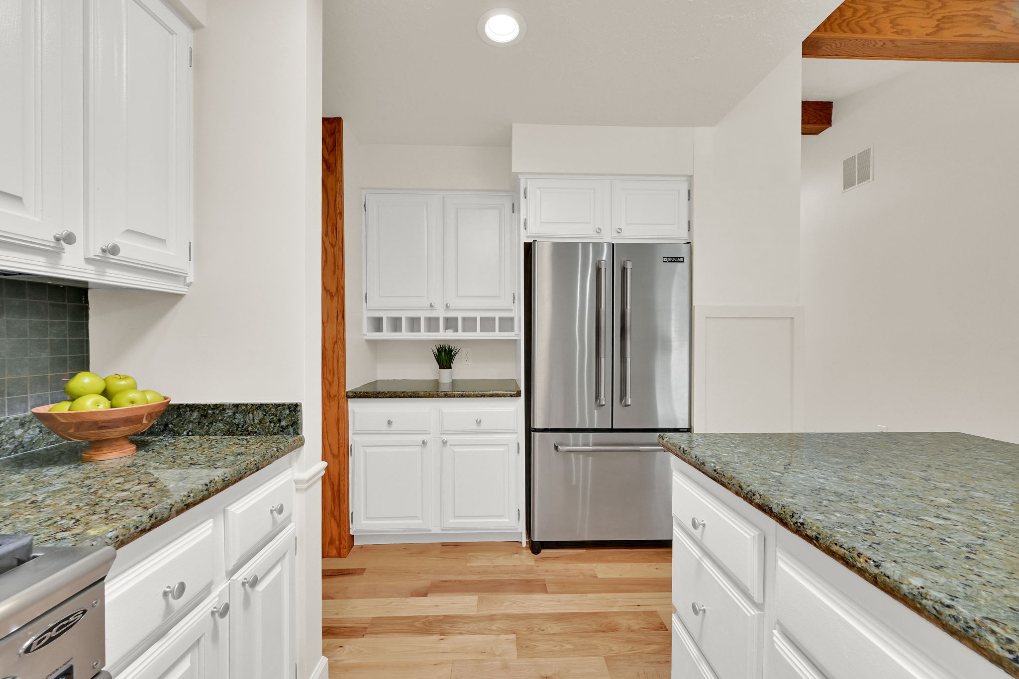 Kitchen featuring extensive white cabinetry, speckled stone countertops, stainless steel French door refrigerator, wood-finish flooring, and exposed wood ceiling beams