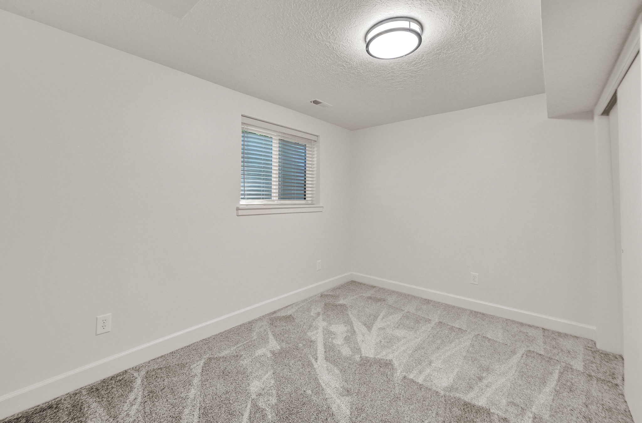 Recessed window with blinds, light gray patterned carpet, and white baseboards