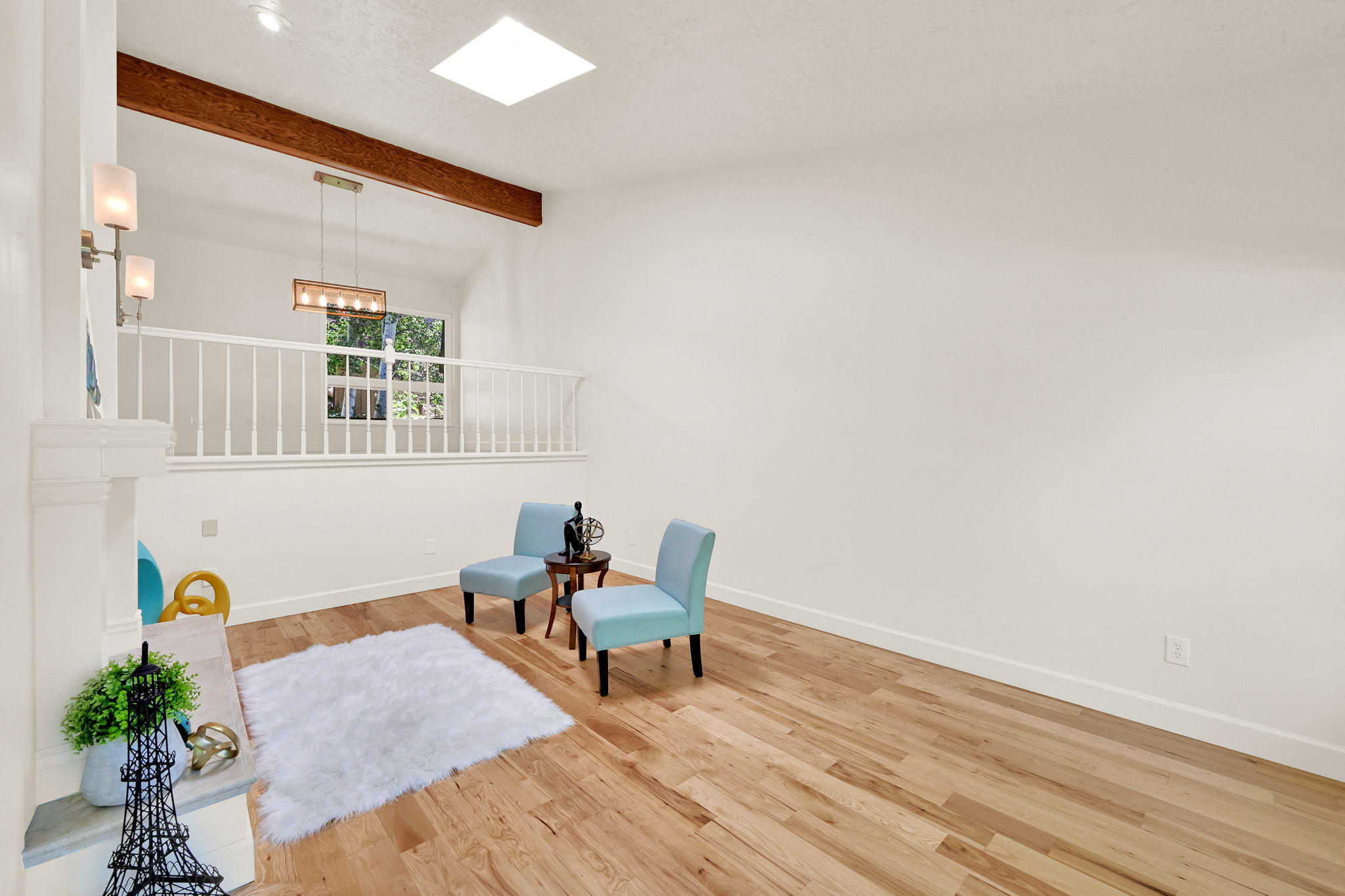 Bright open-concept space featuring wood-finish flooring, a white-painted fireplace surround with a stone top, and high ceilings with an exposed wood beam