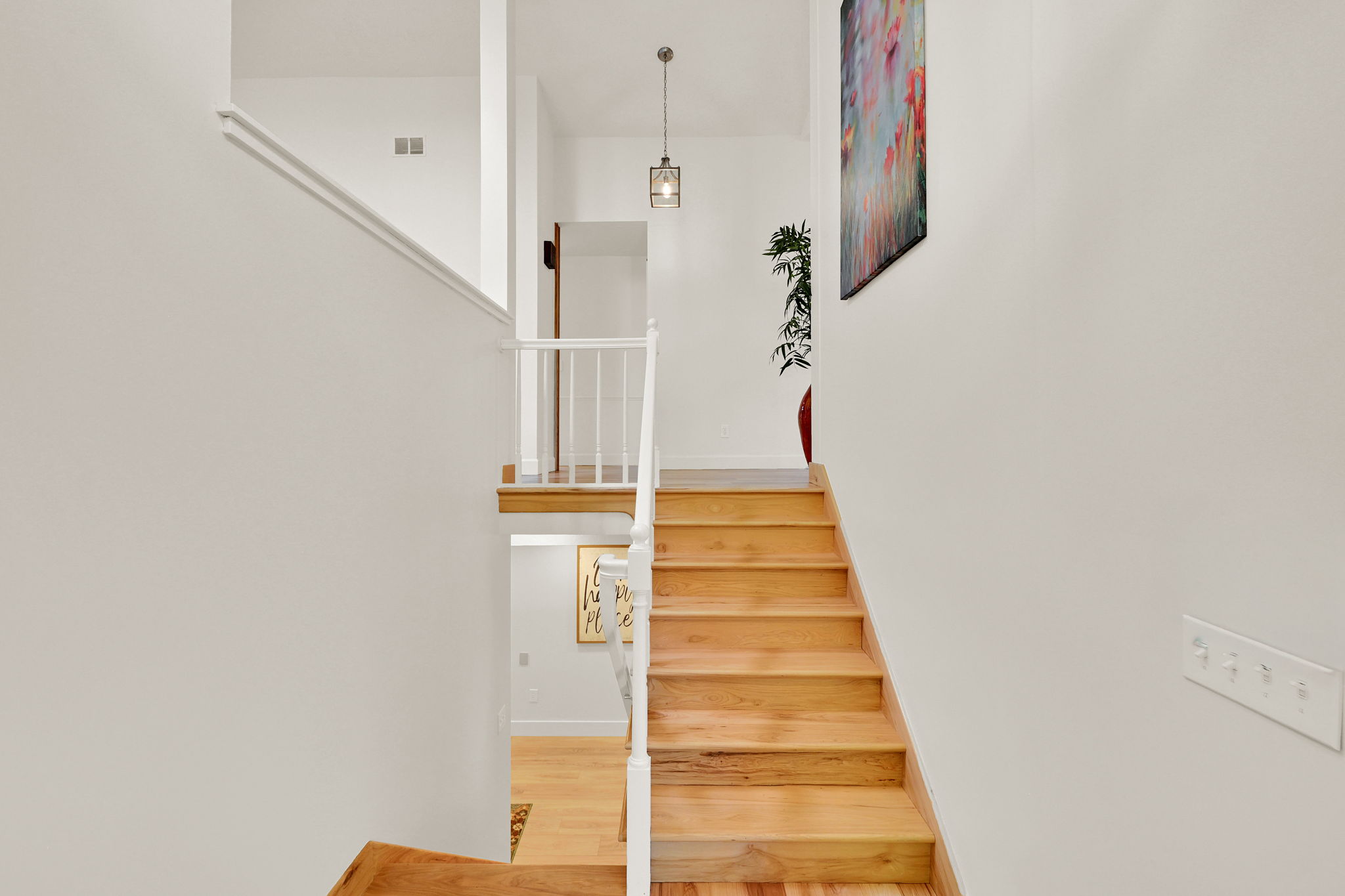 Split-level staircase featuring light wood-finish treads and risers, white railing, and a contemporary pendant light fixture