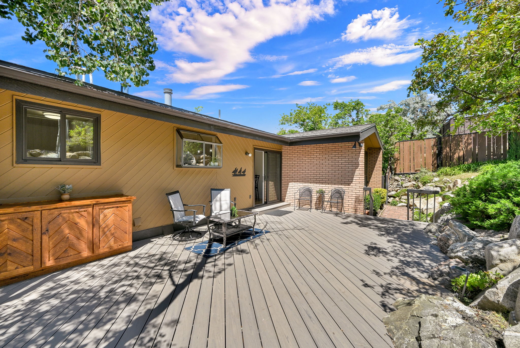 Spacious outdoor deck featuring gray composite decking, a sliding glass door, and a brick exterior accent