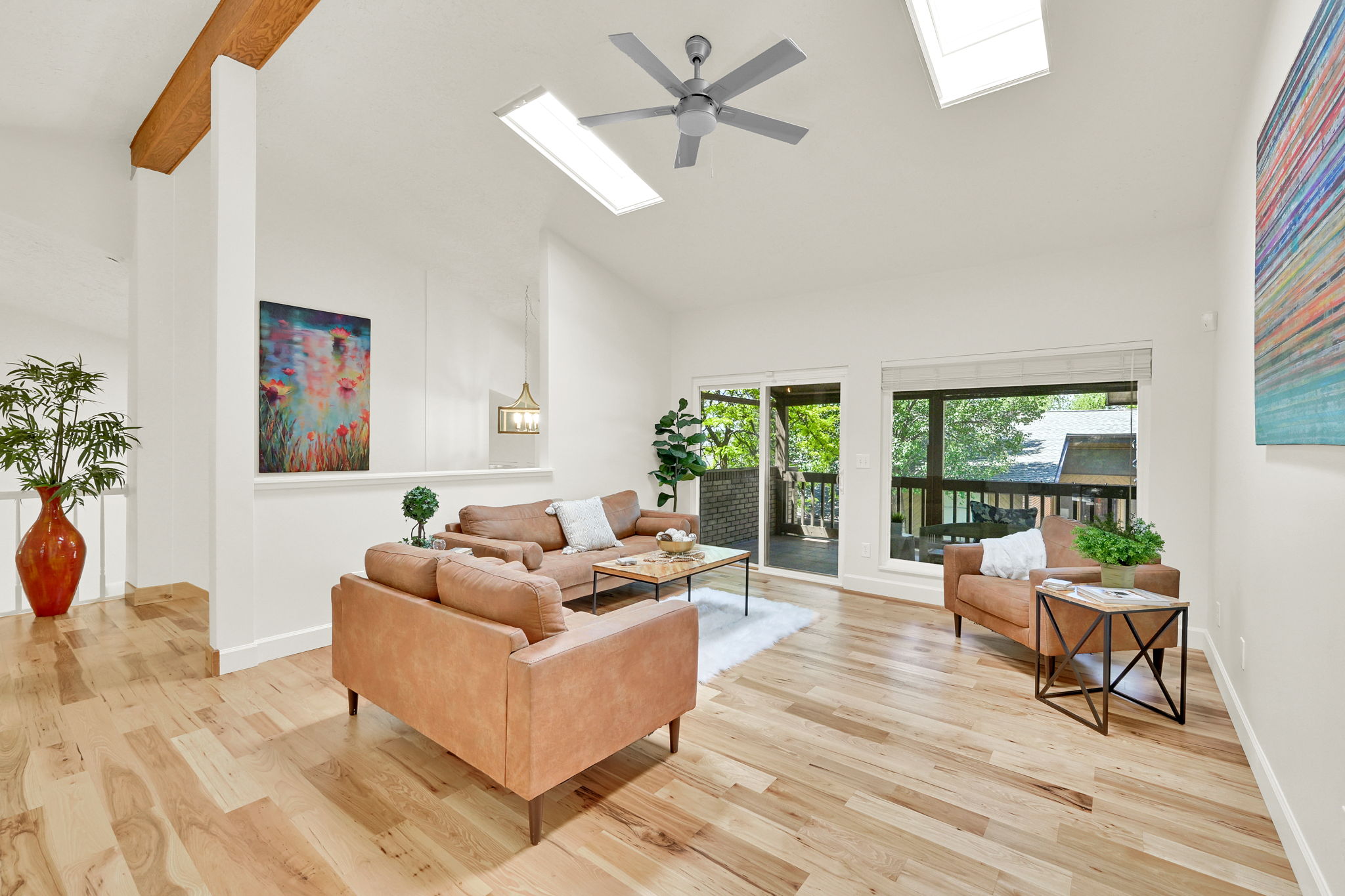 Spacious living area featuring light wood-finish flooring, a vaulted ceiling, and multiple skylights