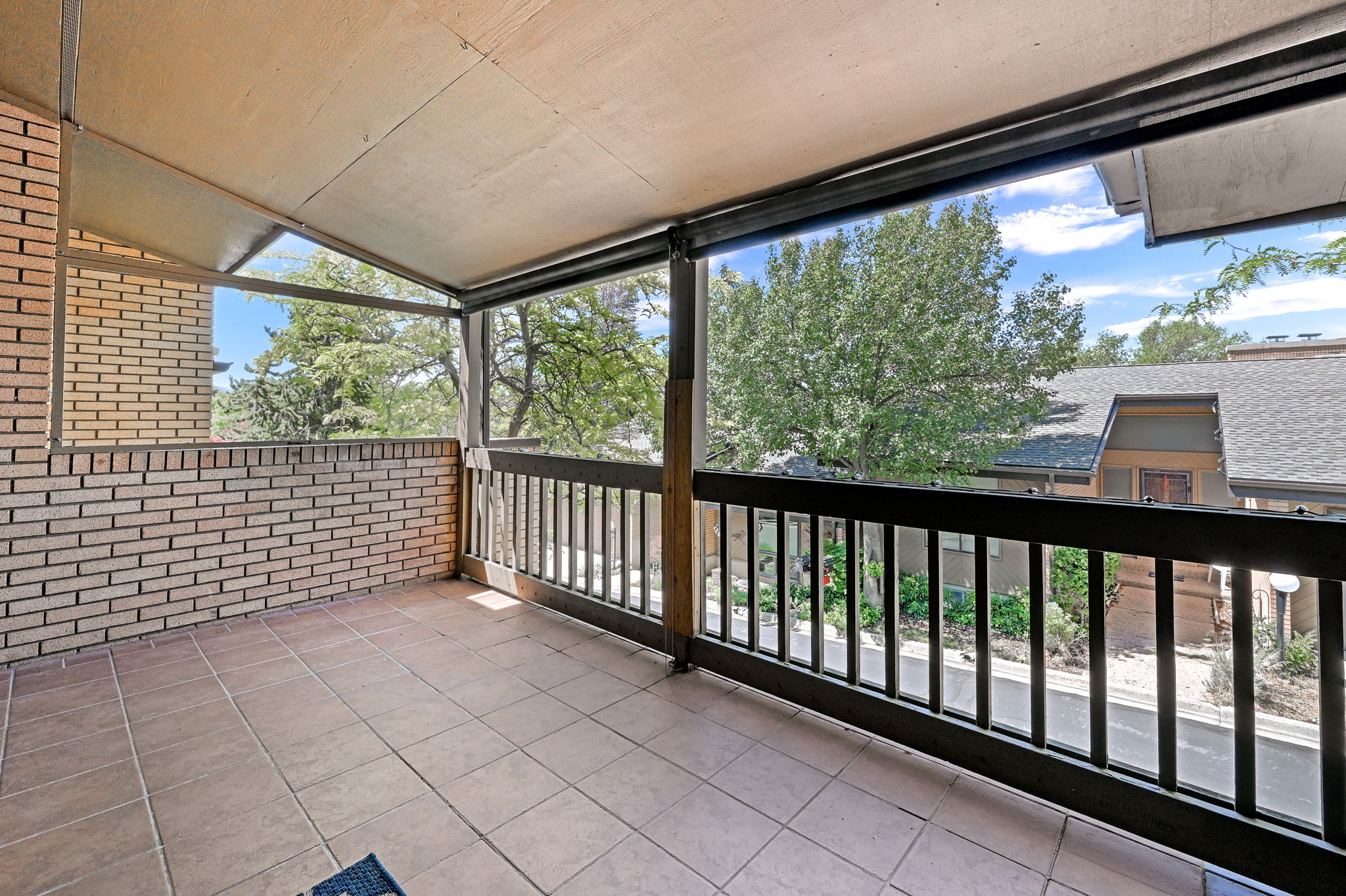 Covered outdoor balcony featuring tile flooring, a brick half-wall, and a wooden railing