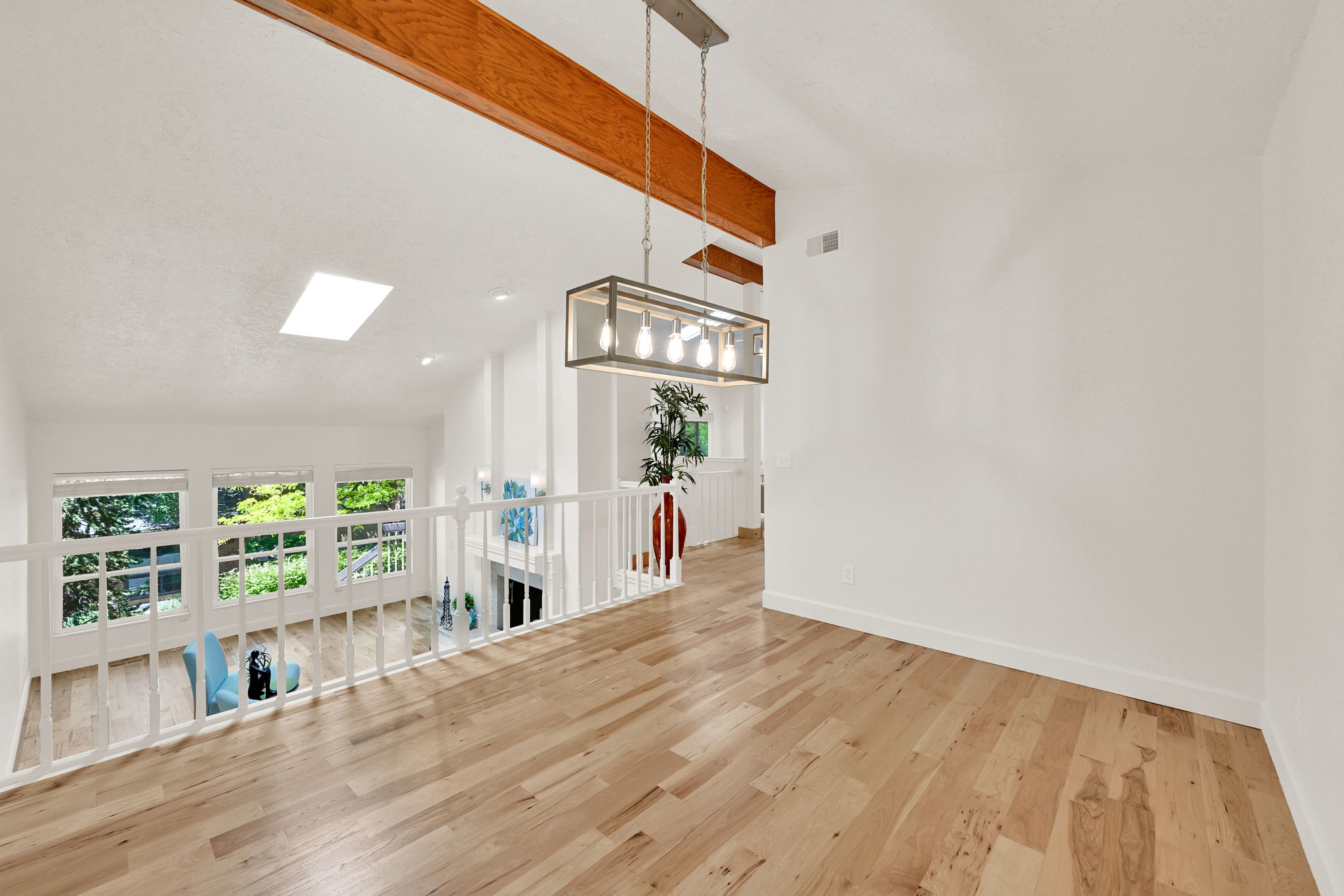 Open concept upper level featuring wood-finish flooring, a skylight, and a contemporary linear chandelier