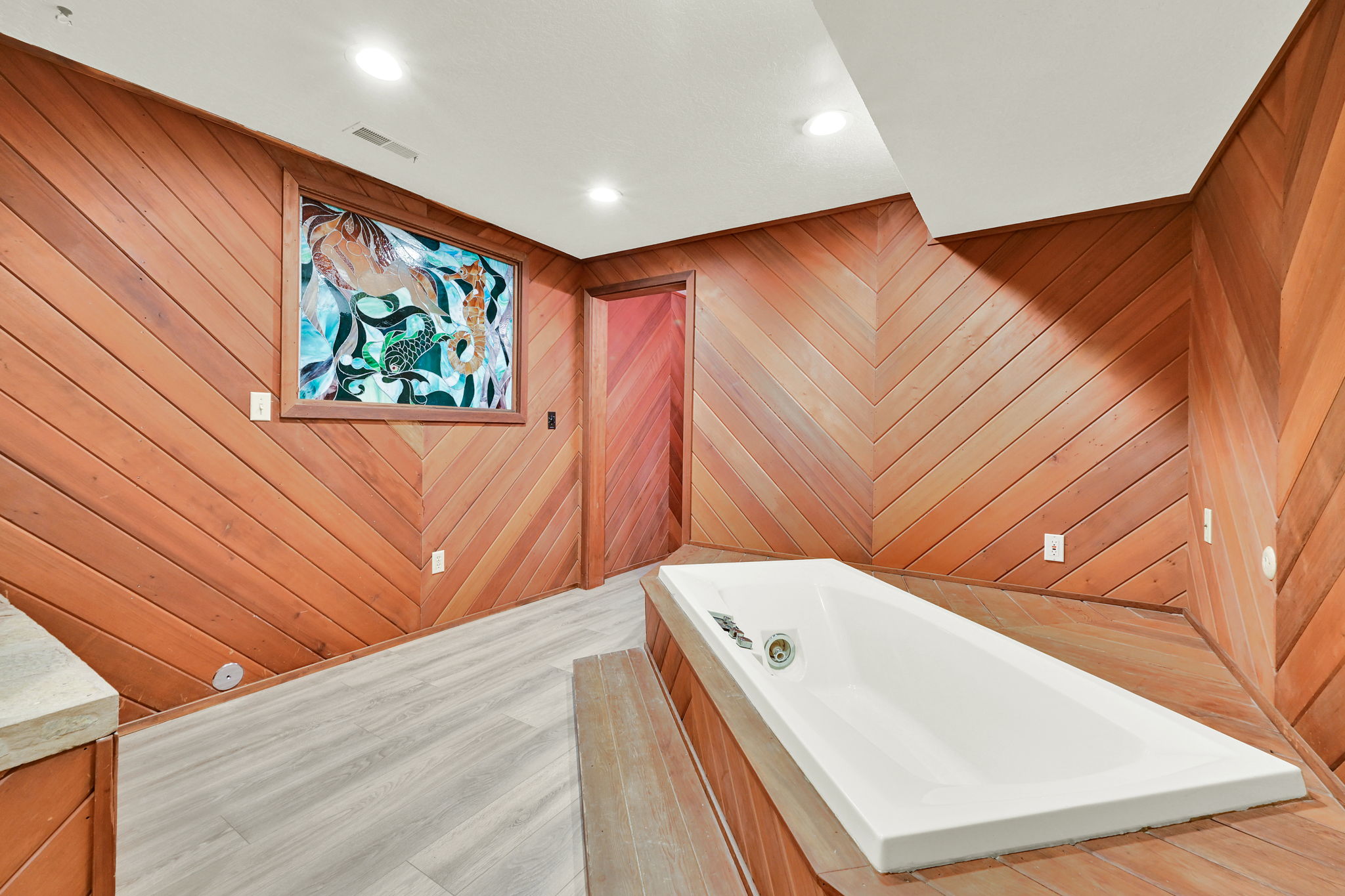 Soaking tub set within a wood-paneled surround, featuring chevron-patterned wood paneling on the walls and ceiling