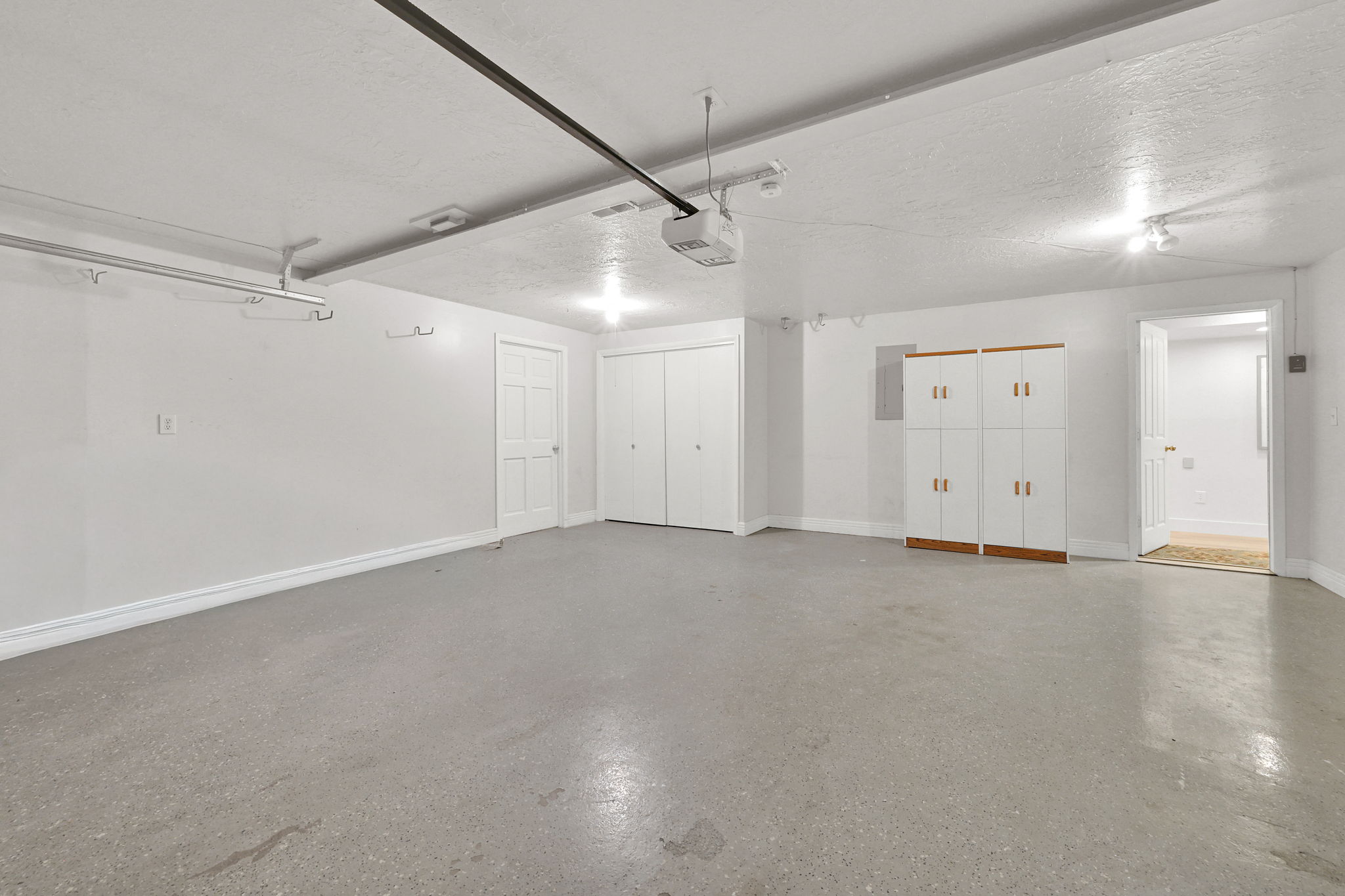 Spacious utility room featuring concrete flooring, track lighting, built-in storage cabinets with wood-finish bases, and two paneled doors