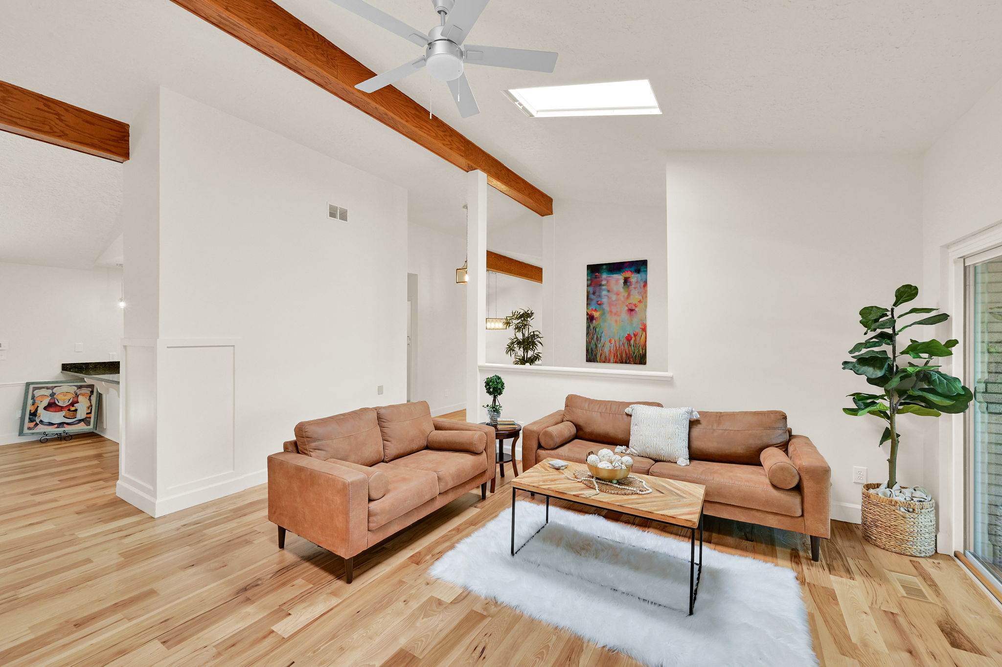 Spacious living area featuring exposed wood beams, wood-finish flooring, and a ceiling fan