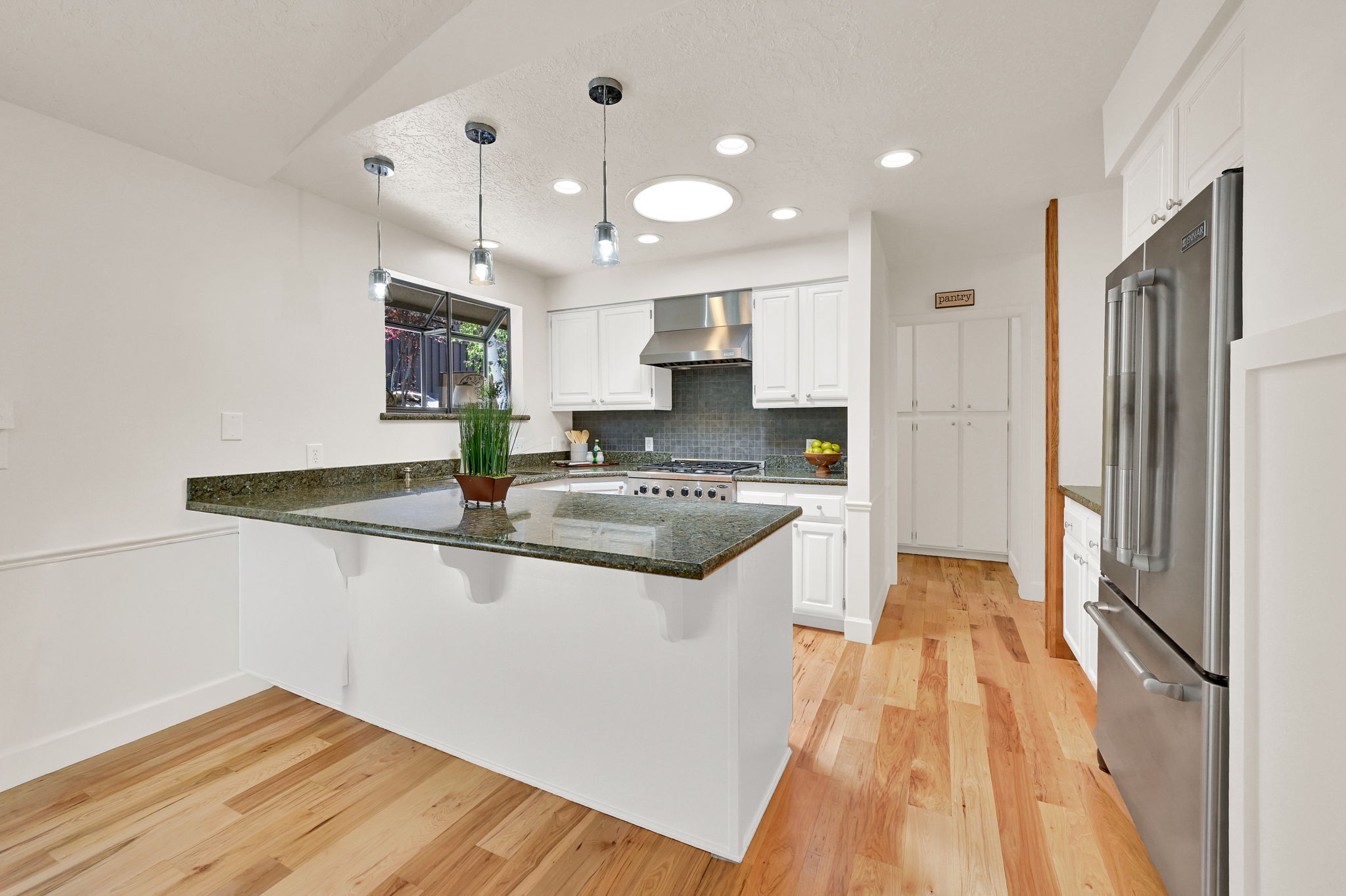 Kitchen featuring a breakfast bar with stone countertop, wood-finish flooring, white cabinetry, stainless steel appliances, and recessed lighting