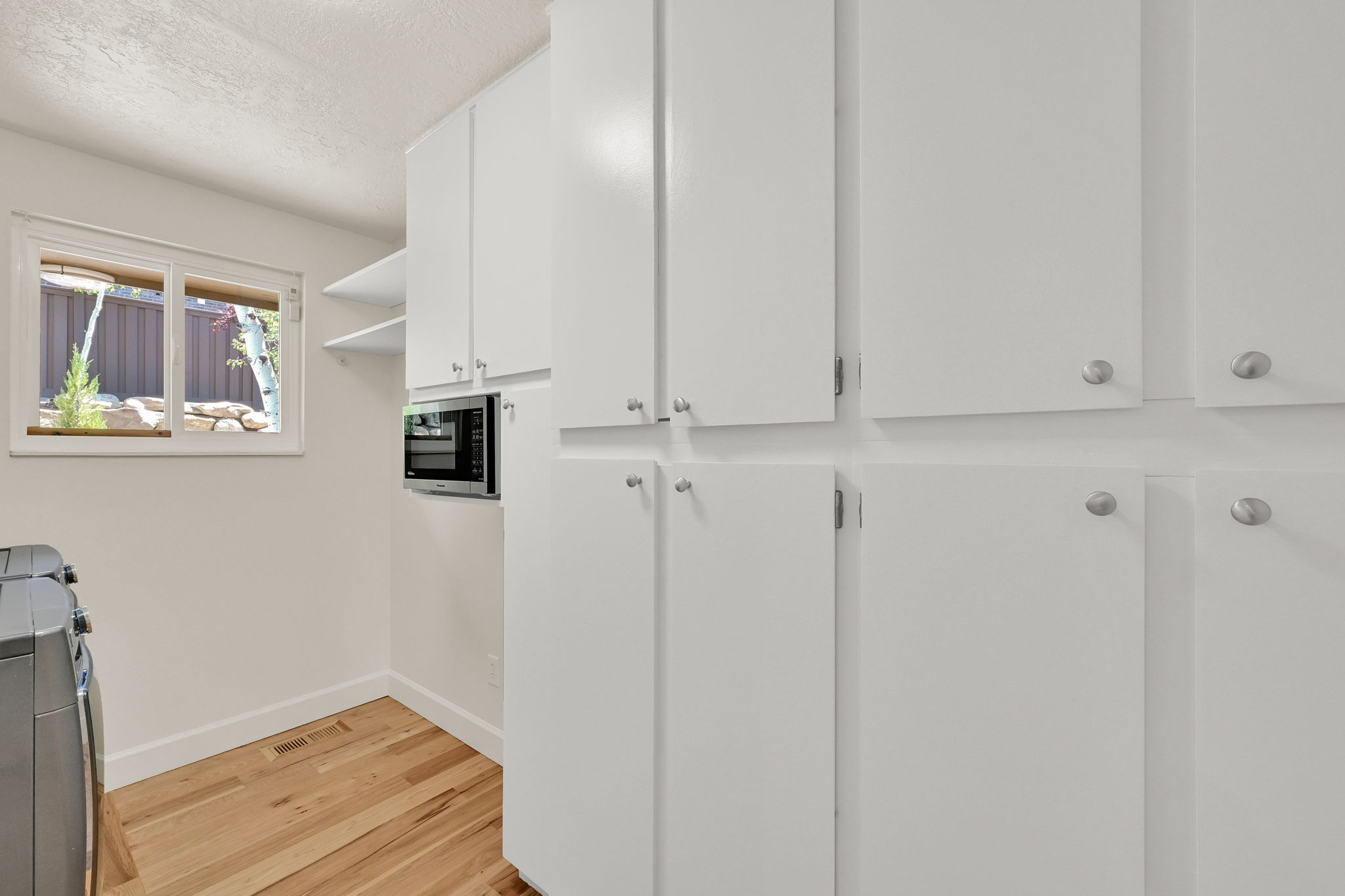Utility area featuring extensive white cabinetry with brushed nickel hardware, light wood-finish flooring, and a built-in microwave