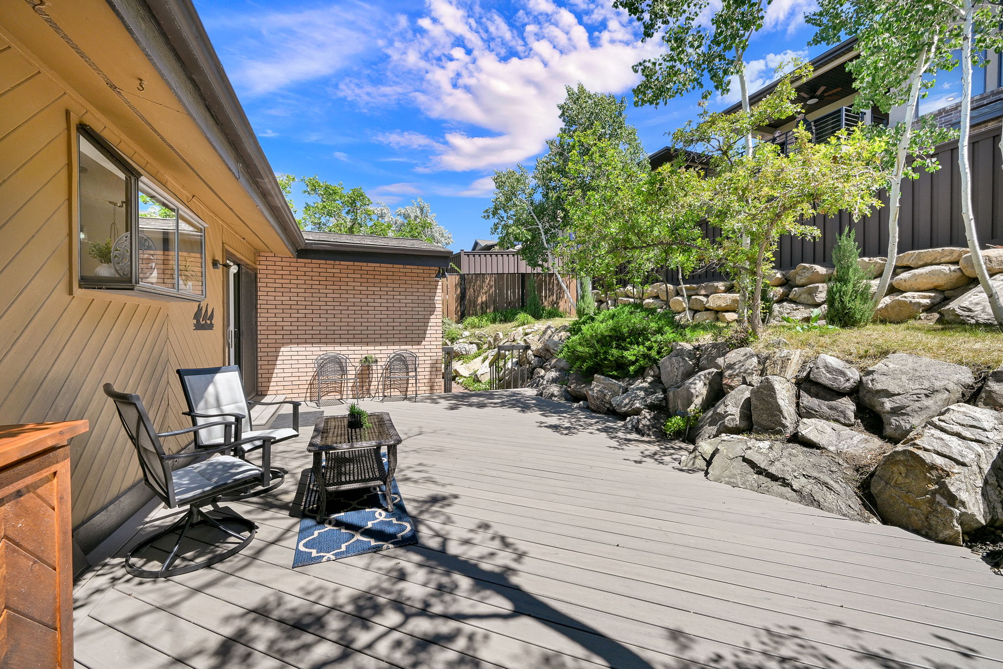 Expansive outdoor deck with composite decking, a brick facade, and a natural rock retaining wall