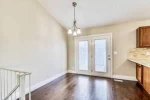 Dining area featuring vaulted ceilings, dark wood-finish flooring, white baseboards, and a contemporary chandelier