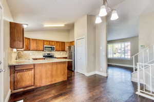 Kitchen featuring wood cabinetry, stainless steel appliances, and stone countertops with a complementary backsplash