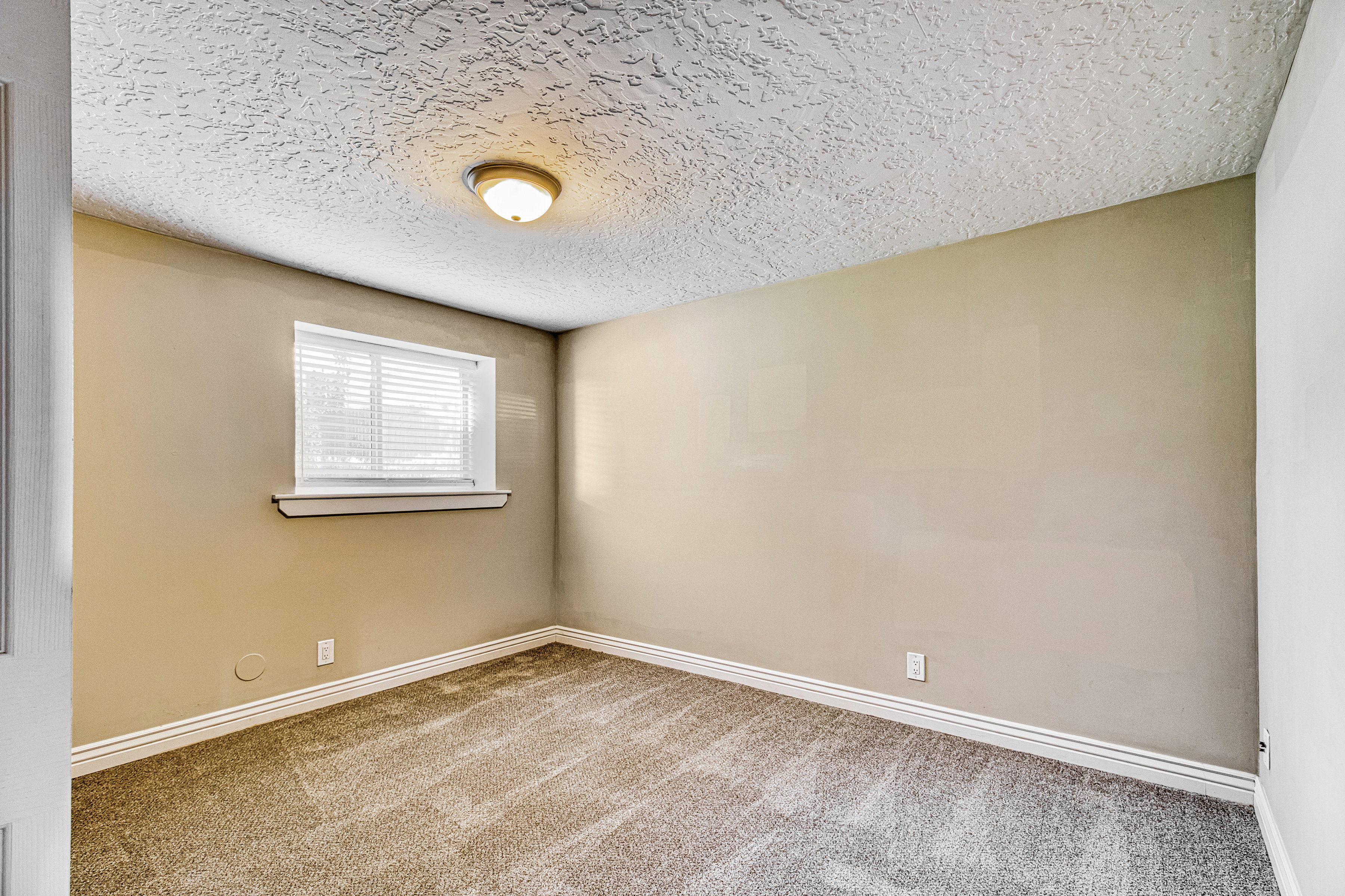 Carpeted room featuring a single window with horizontal blinds, neutral wall paint, white baseboards, and a semi-flush mount ceiling light