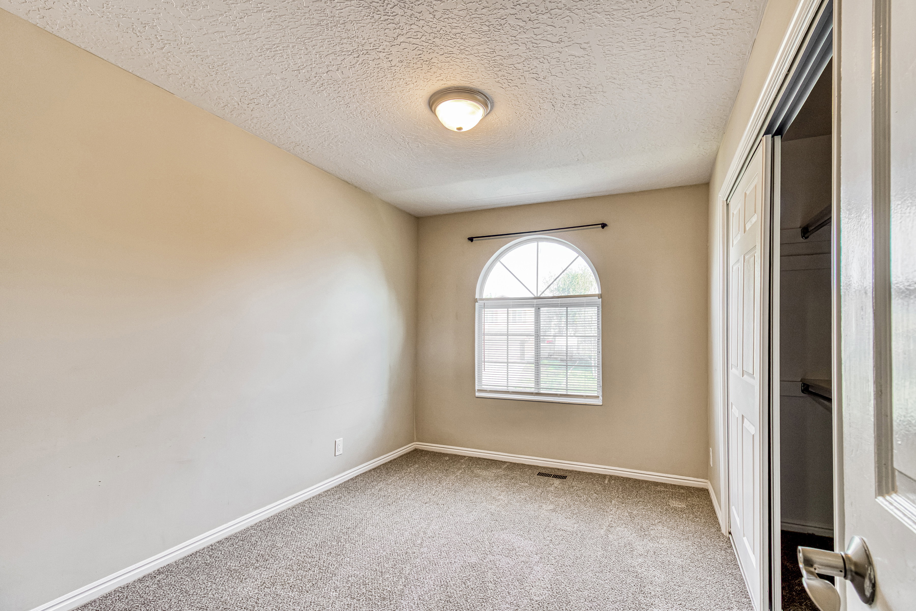 Room featuring an arched window, neutral wall paint, gray carpet flooring, white baseboards, and a built-in closet with bi-fold doors
