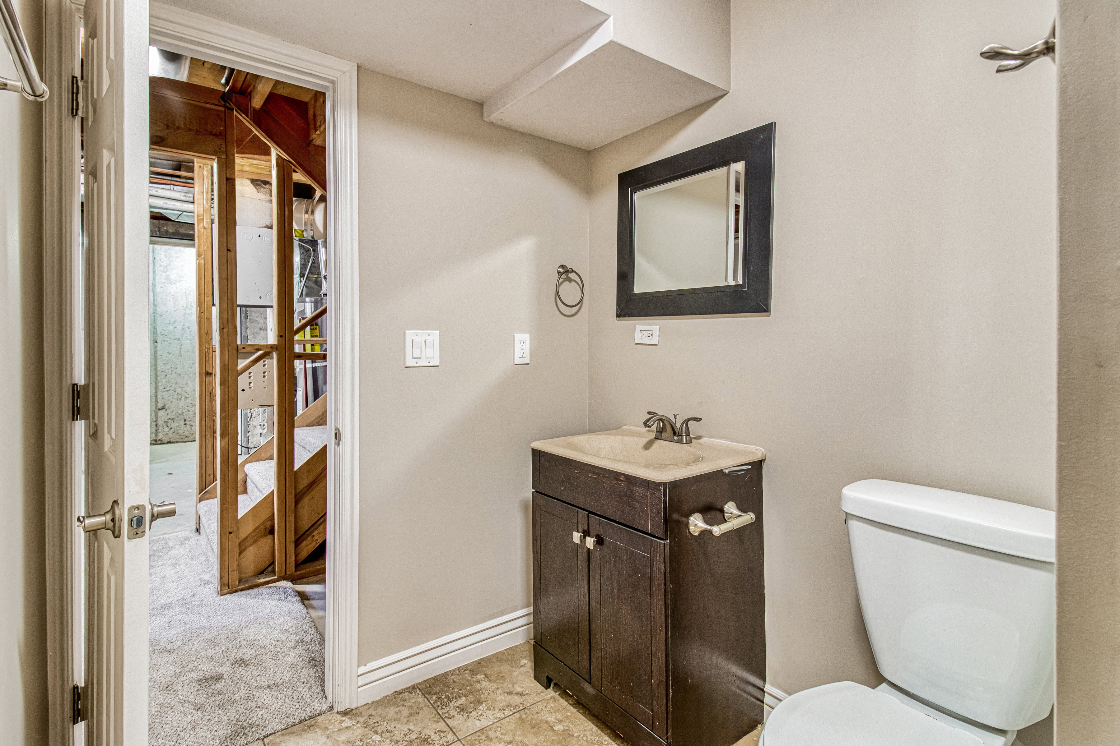 Bathroom featuring a dark wood-finish vanity with an integrated sink, framed mirror, and tile flooring