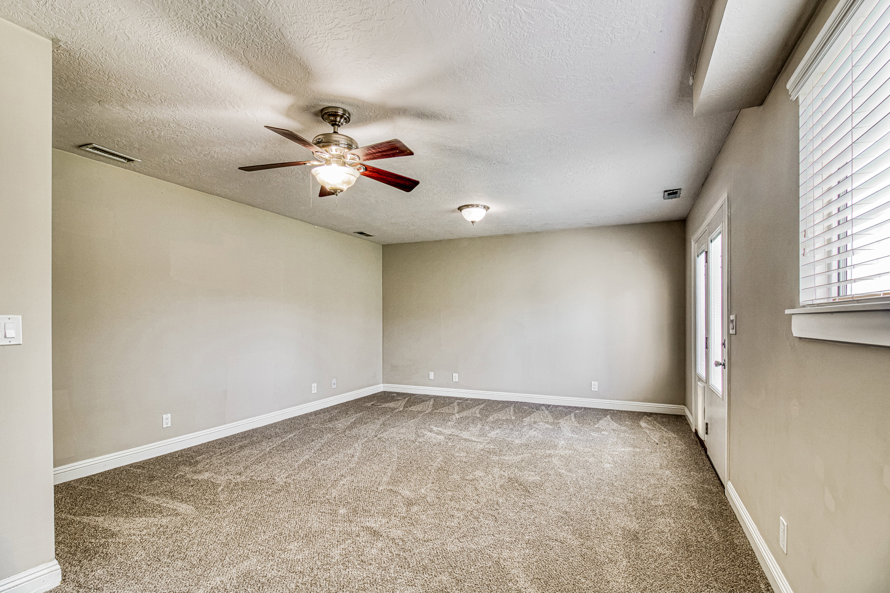 Spacious room featuring neutral carpeting, light-toned walls, and white baseboards