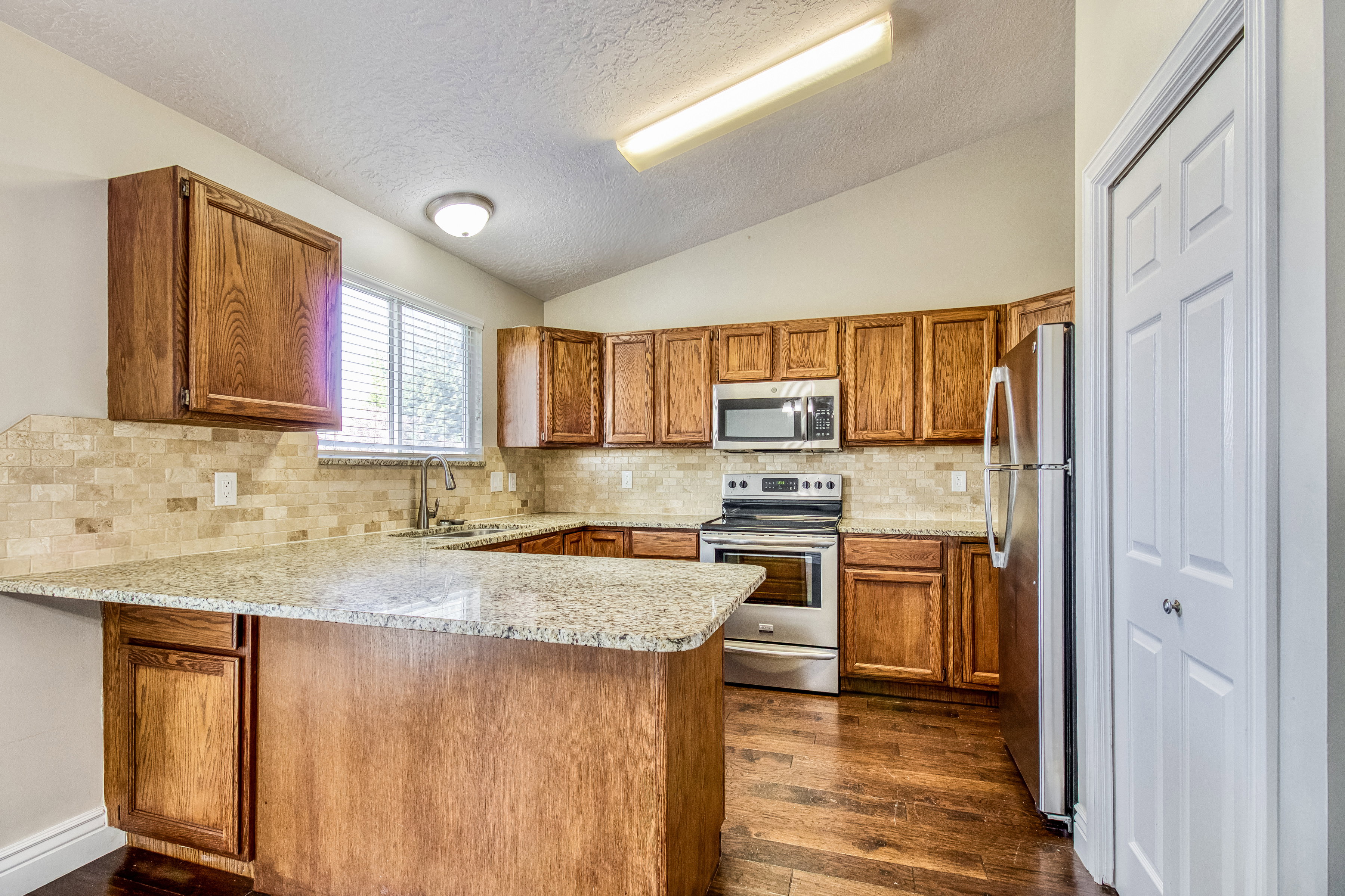 Kitchen featuring wood cabinetry, stainless steel appliances, granite countertops, and a tiled backsplash