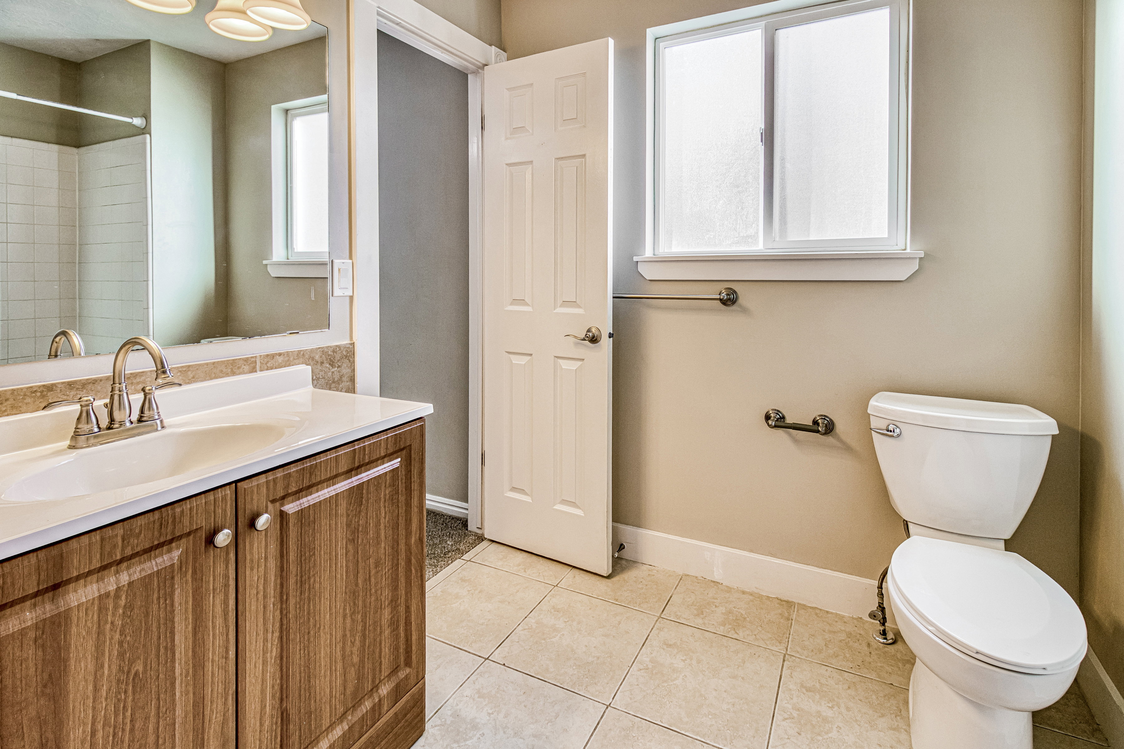 Bathroom featuring a wood-finish vanity with a white countertop and integrated sink, a large mirror, tiled flooring, and a window with privacy glass