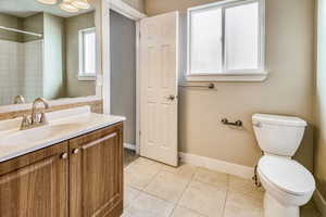 Bathroom featuring a wood-finish vanity with a white countertop and integrated sink, a large mirror, tiled flooring, and a window with privacy glass