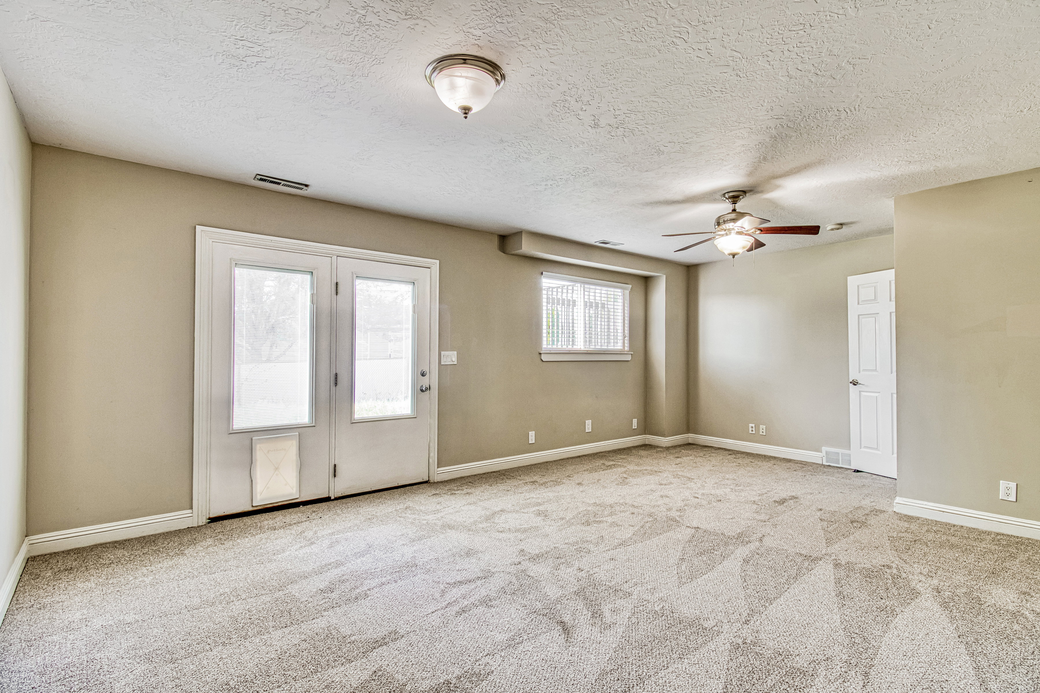 Spacious room featuring neutral carpeting, a ceiling fan with integrated lighting, and a double-door exterior entry with an integrated pet door